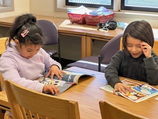 Two kindergarten students sit at a table, reading books.