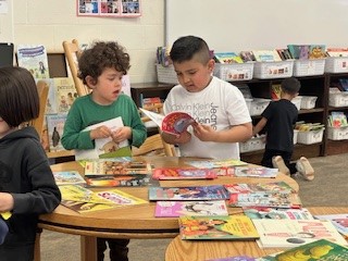 Two kindergarten students look though books laid out on a table. 