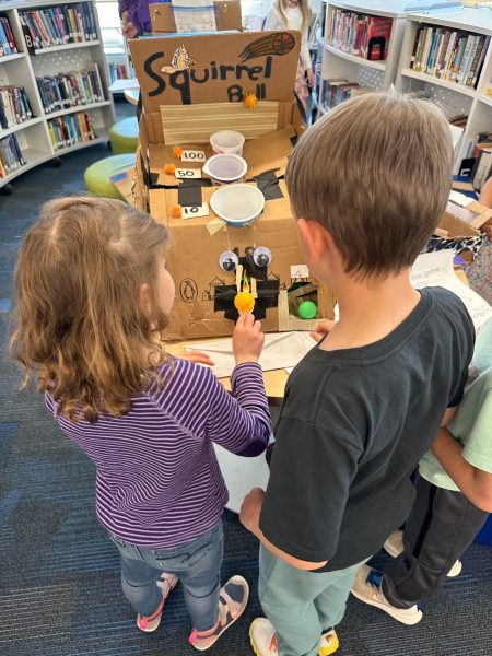 A kindergarten student launches a ping pong ball, trying to land it in a cup to score points in the arcade game Squirrel Ball.