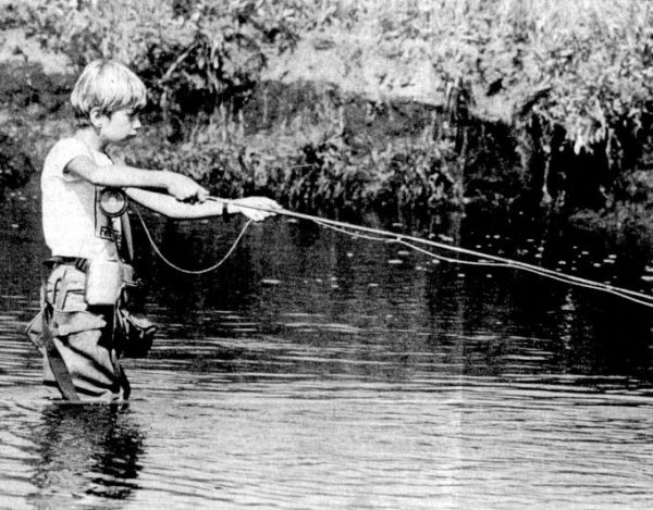 A boy in hip waders fishes in a creek