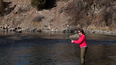 An angler stands in shallow water with a fishing rod and a cast fishing line.