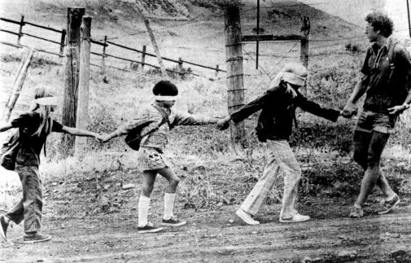 A camp counselor leads a group of blindfolded children holding hands