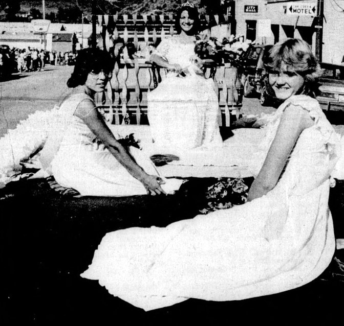 Three women in gowns sit on a parade float.