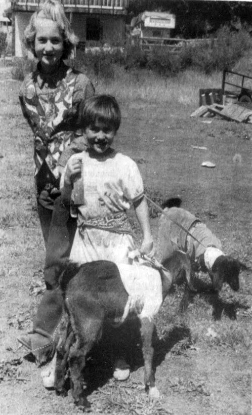 A girl and boy show off their pet goats wearing clothes