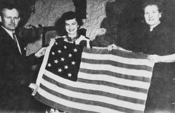 A man and two women hold up a 13-star American flag.