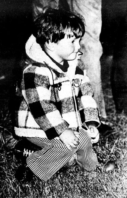 A little boy in a plaid jacket sits on a football