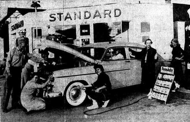 A group of young women help tune up a car at a gas station.
