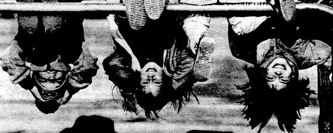 Three children hang upside down at a playground.