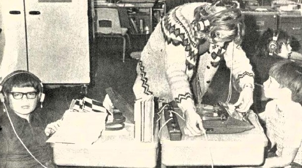 A teacher sets up listening stations for two boys.