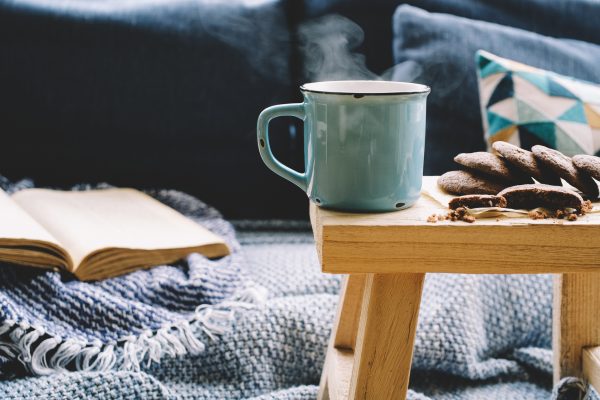 Cup of hot drink on wooden table. Living room interior with blue sofa on background.