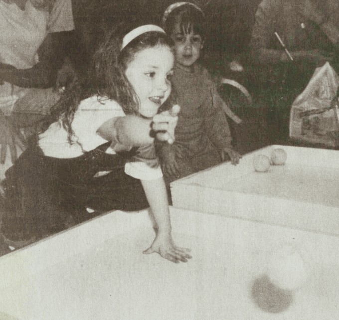 A young girl throws a skeeball while another girl looks on.