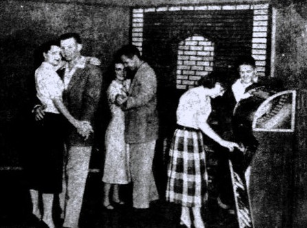 Two young couples dance while a third couple plays the jukebox.