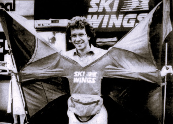 A man wears wings attached to ski poles.