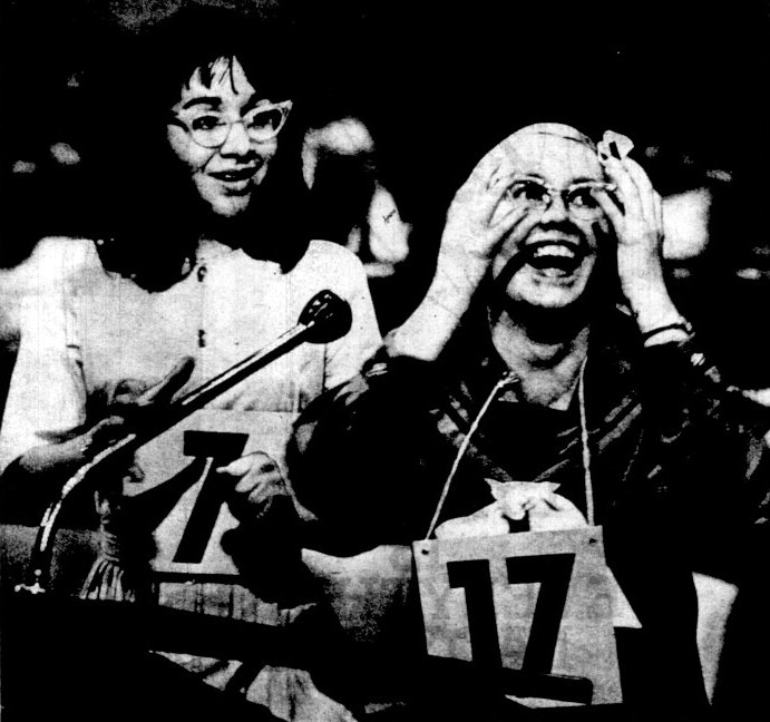 A girl puts her hands to her face in excitement while a second girl looks on.