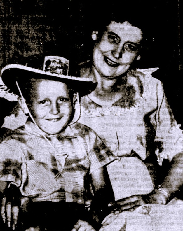 A young boy in a western-style hat sits with his mother.