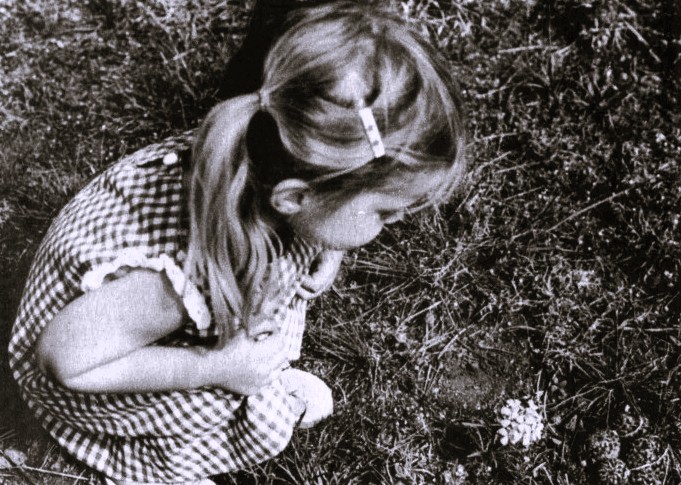 A young girl crouches to look at a flower.