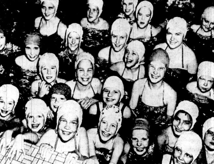 A large group of girls wearing swim caps gather in a pool