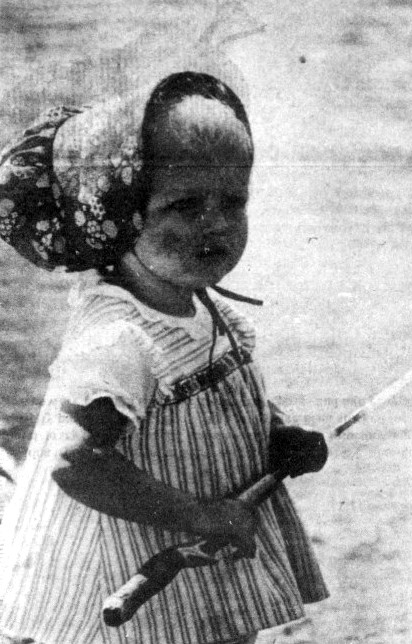 A toddler wearing a bonnet holds a fishing pole.