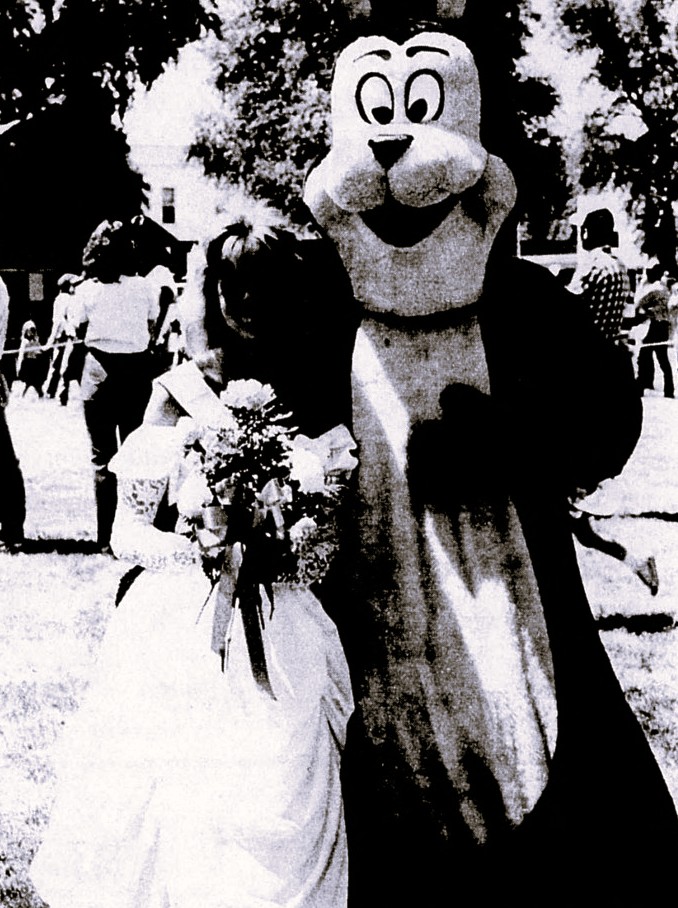 A woman in a wedding dress stands next to a person in a bear costume.