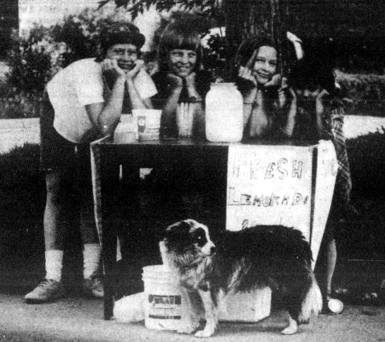 4 children and a dog pose next to a lemonade stand.