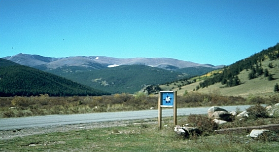 A paved highway cuts through a high alpine landscape with the columbine sign denoting a Scenic and Historic Byway.