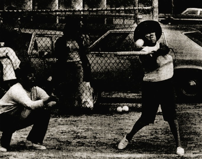 A woman swings at a softball.