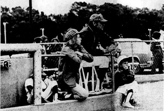 A coach and 3 baseball players watch the game from the dugout.