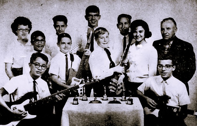 10 young guitar players pose with a table of trophies.
