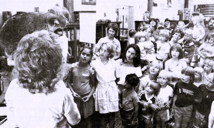 A man shows a raccoon to a large group of children.