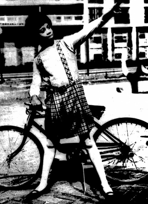 A girl wearing a jumper poses in front of a bike.