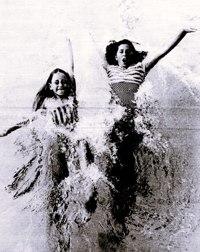 Two girls go down a water slide.