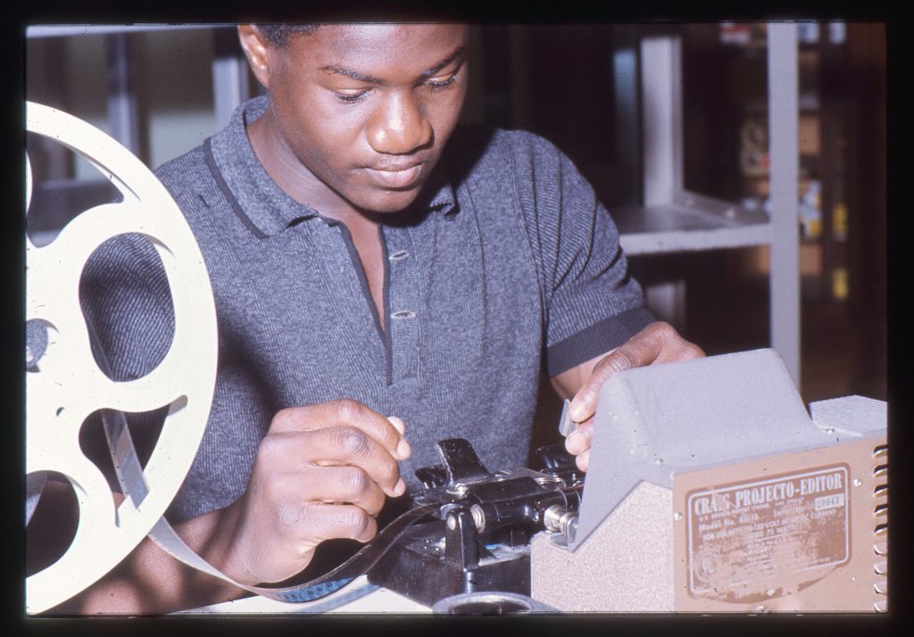 A high school student feeds a film reel through an editing machine.