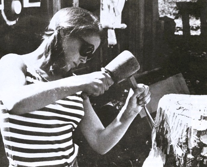A young woman sculpts with a hammer and chisel