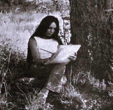 A woman sits under a tree and draws in a notebook.
