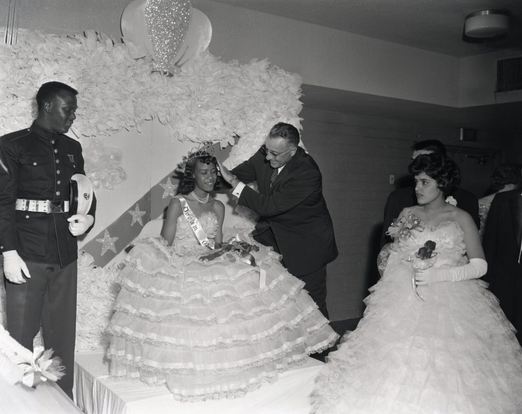 Image of two young women in prom dresses.  One is being crowned.