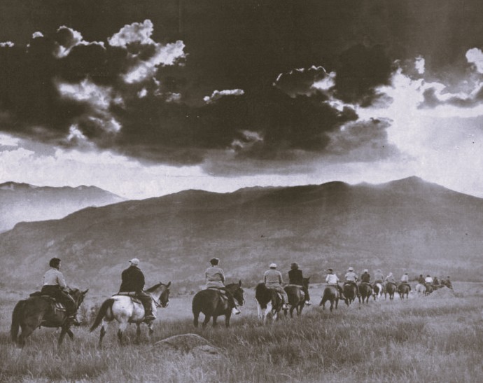 A group of people ride horses single-file towards a mountain.
