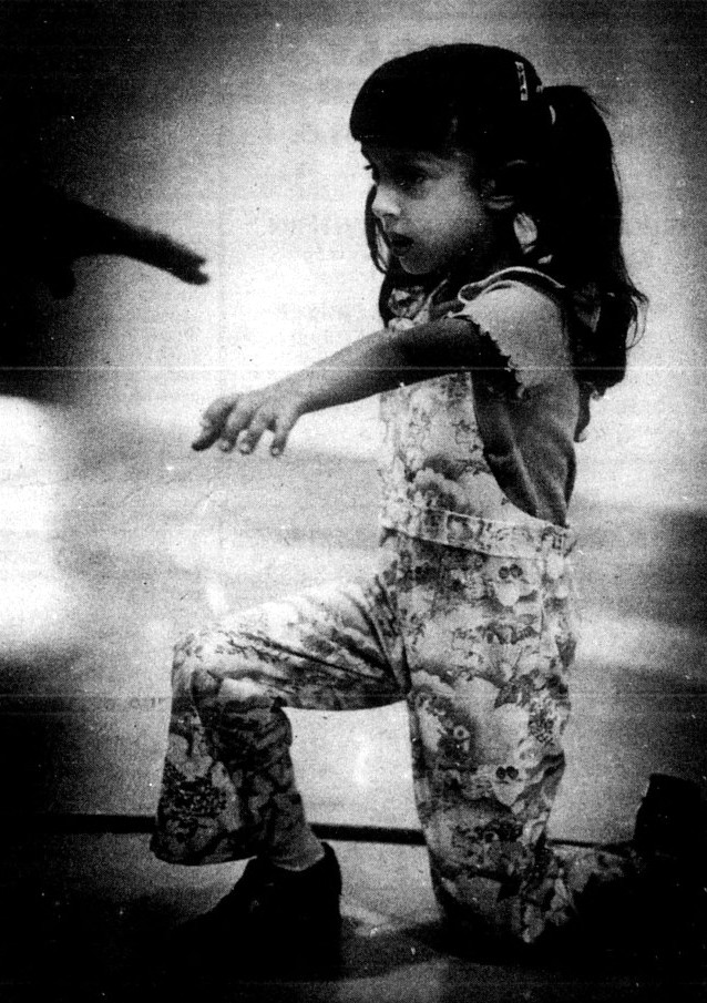 A girl demonstrates that she can kneel with one arm raised.