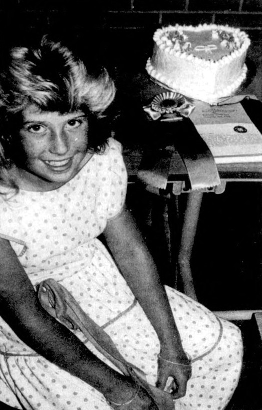 A girl sits beside an award-winning cake she decorated.