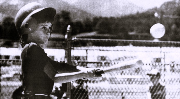 A girl wearing a helmet swings at a baseball.