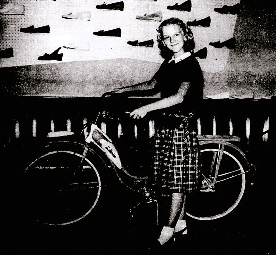 A girl poses next to a bike and in front of a wall of shoes.