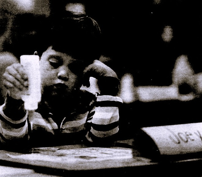 A little boy rests his head on one hand while he uses glue with the other.