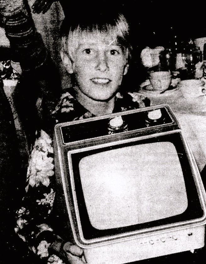 A boy in a floral shirt holds a television.