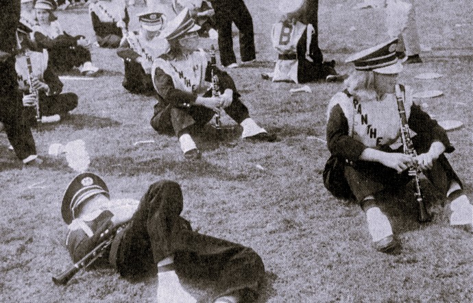 The clarinet section of a marching band rests on the grass.