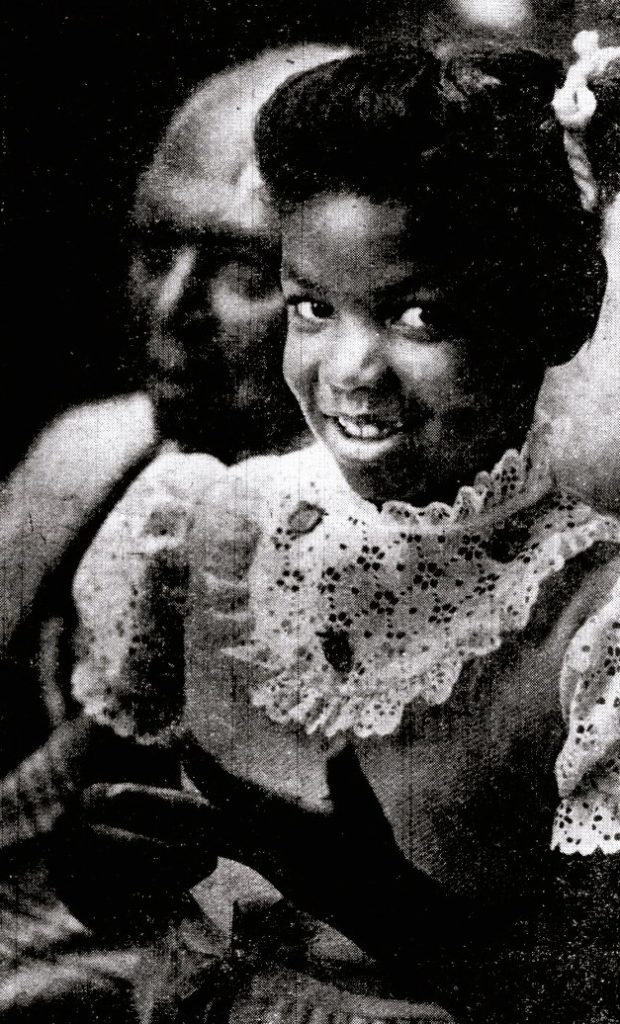 A little girl in a dress sits with her grandfather.