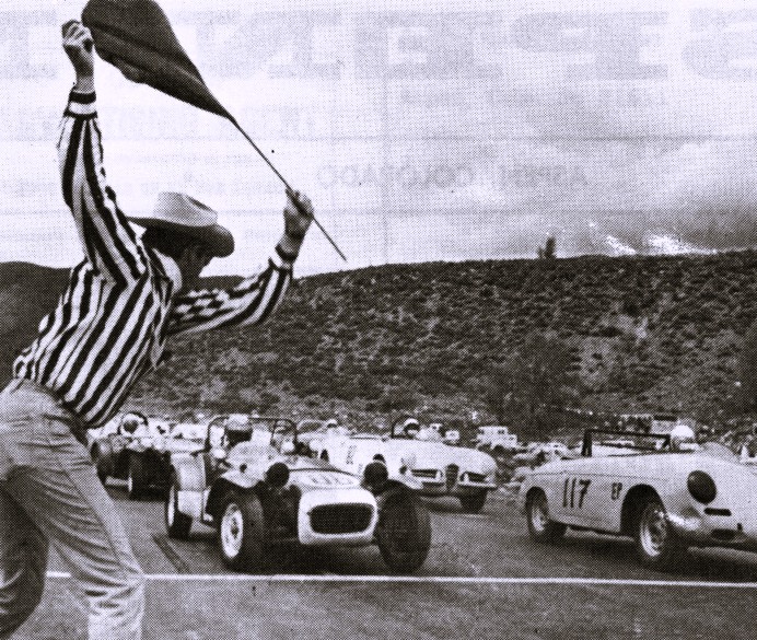 A man waves a flag at the starting line of a car race.