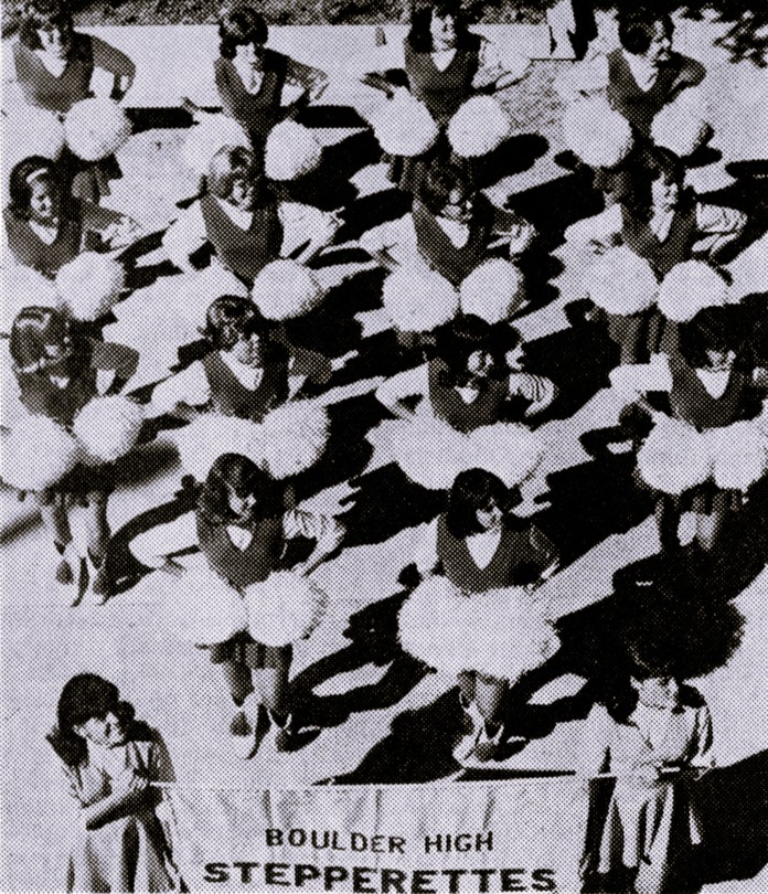 A squad of cheerleaders marches with their pom-poms.
