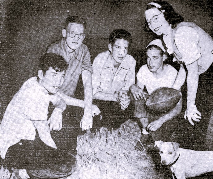 A young woman, four young men, and a dog pose with a football.