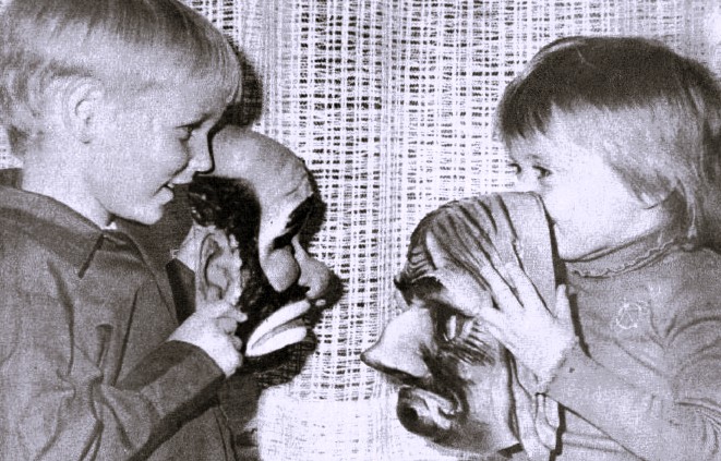 Two young children hold up Halloween masks.
