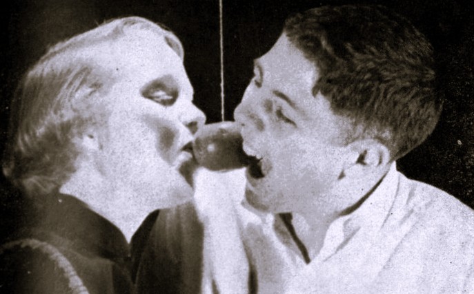 A boy and a girl attempt to bite the same apple on a string.