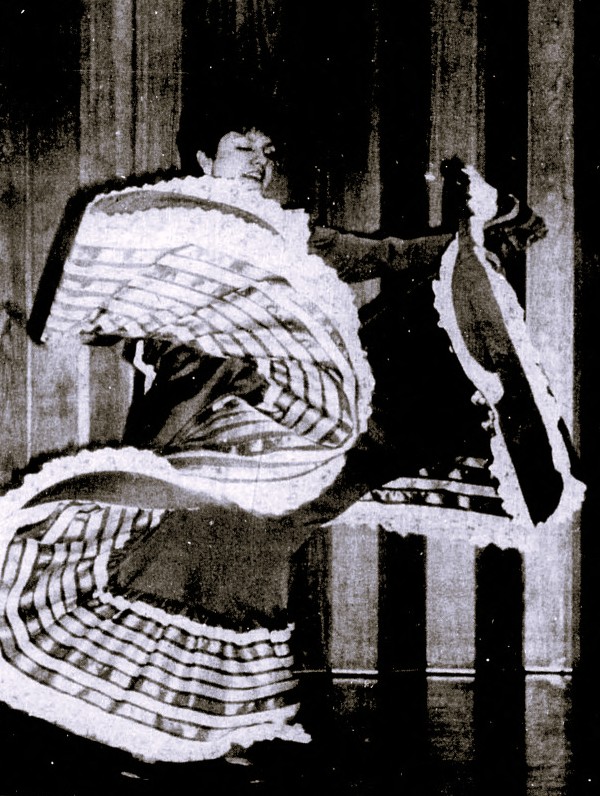 A woman performs a dance in a traditional Mexican dress.